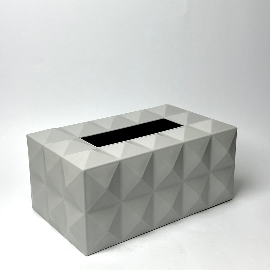 A rectangular tissue box cover with a geometric faceted design in light gray, featuring a black opening for tissues, set against a plain white studio background.