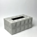 A rectangular tissue box cover with a geometric faceted design in light gray, featuring a black opening for tissues, set against a plain white studio background.