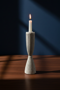 A lit white candle in a ribbed ceramic holder with a flared base, placed on a wooden table against a dark blue background with dramatic shadows.