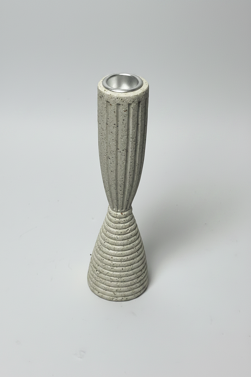 A modern, sculptural candle holder made of textured concrete with a flared ribbed base and a fluted neck, featuring a silver metal inner cup, set against a neutral light gray background.