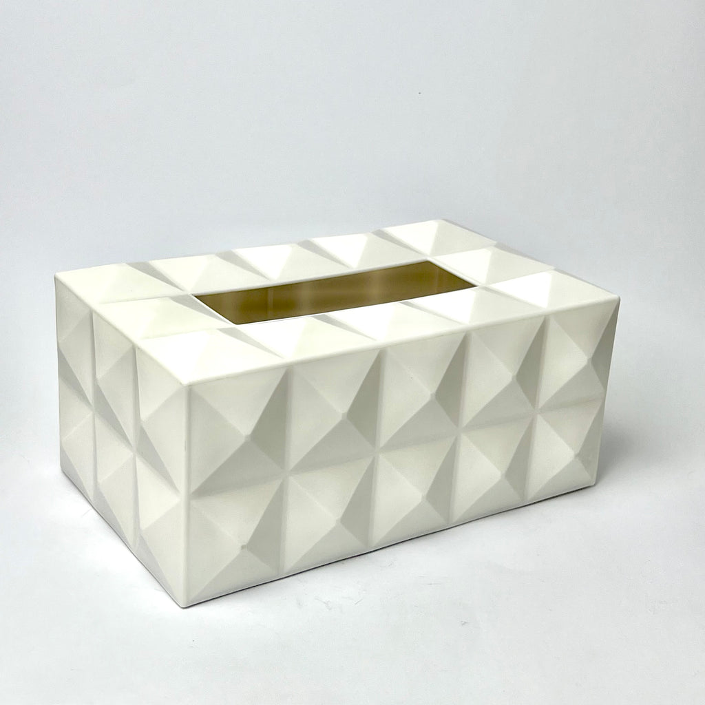 A white geometric tissue box cover with a faceted, 3D diamond pattern and a gold metallic inner slot, photographed on a light gray background.