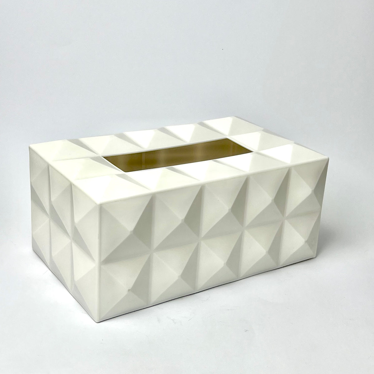A white geometric tissue box cover with a faceted, 3D diamond pattern and a gold metallic inner slot, photographed on a light gray background.